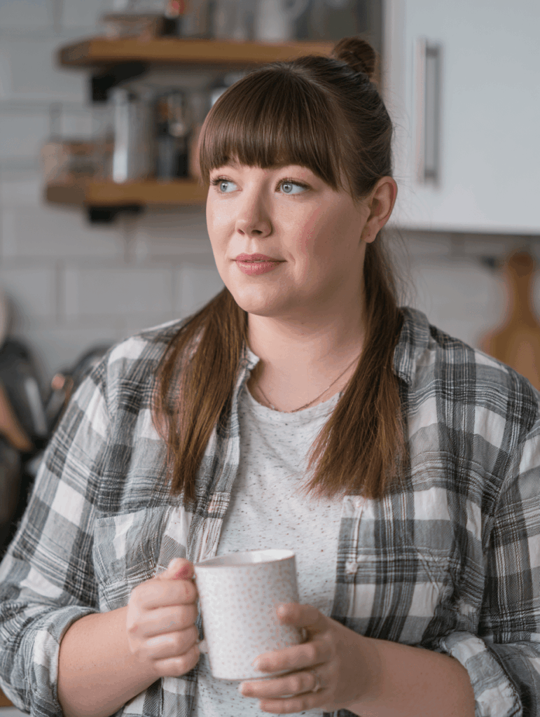 Porträt einer rundlichen Frau mit Tasse in der Küche, ruhiger Blick in die Kamera.